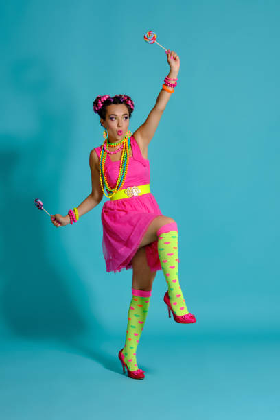 istock Lovely girl with a multi-colored braids hairstyle and bright make-up, posing in studio against a blue background, holding a lollipop in her hand 1174973663