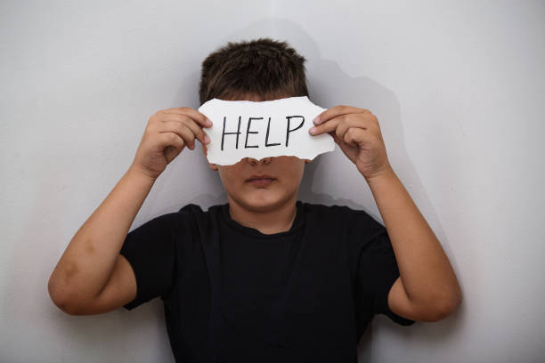 ajuda, adolescente com sinal da ajuda. menino que prende um papel com a inscrição. o miúdo que prende a folha de papel com ajuda da palavra no fundo cinzento da parede. - stop child stop sign child abuse - fotografias e filmes do acervo