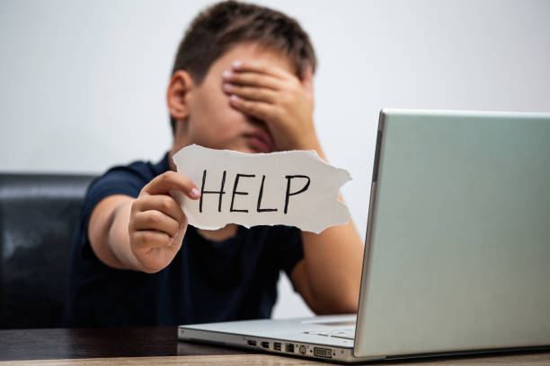 istock Sad and scared young boy with computer laptop suffering cyberbullying and harassment being online abused by stalker or gossip feeling desperate and humiliated in cyber bullying concept. 1174974076