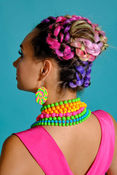 istock Lovely girl with a multi-colored braids hairstyle and bright make-up, posing in studio against a blue background 1174974302