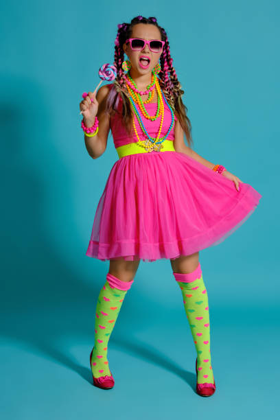 istock Lovely girl with a multi-colored braids hairstyle and bright make-up, posing in studio against a blue background, holding a lollipop in her hand 1174974431