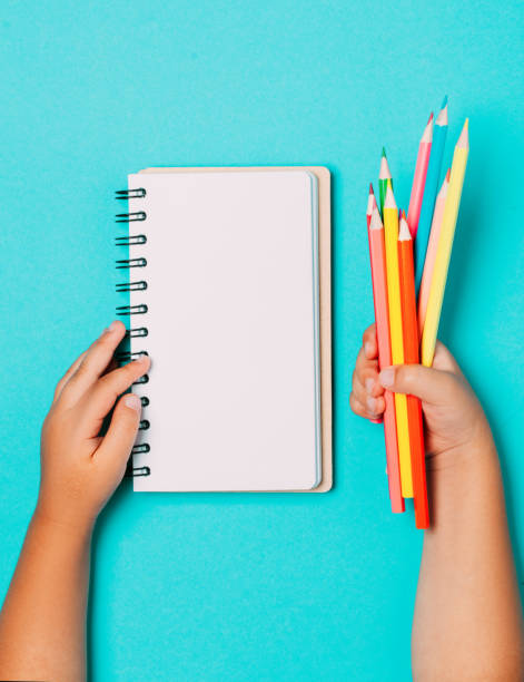 istock School supplies and stationery with children hand writing in empty notebook on blue table top view. 1174974480