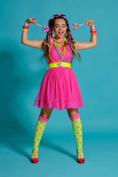 istock Lovely girl with a multi-colored braids hairstyle and bright make-up, posing in studio against a blue background, holding a lollipop in her hand 1174974794