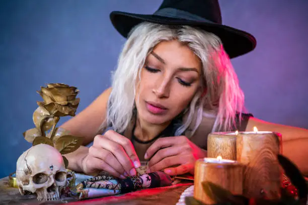 Vodoo girl with nails on table and witch hat with candles and skull
