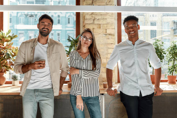 istock Nice coffee! Three cheerful colleagues in casual wear looking at camera while standing in the modern office 1174978790