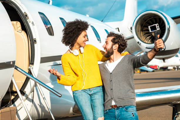 istock Vlogger couple shooting a video together with a small digital camera mounted on a portable tripod next to the nose cone of a private jet parked on an airport runway 1174980841