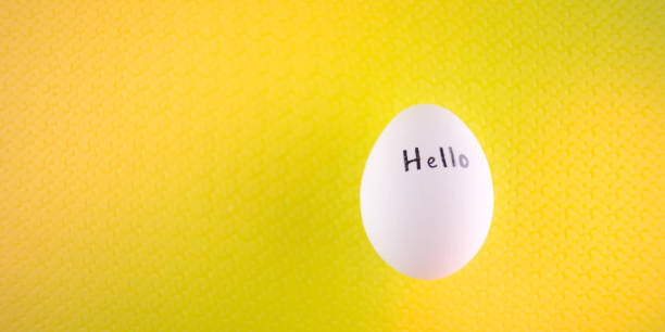 istock White chicken egg with black inscription hello on a yellow background. 1174983440