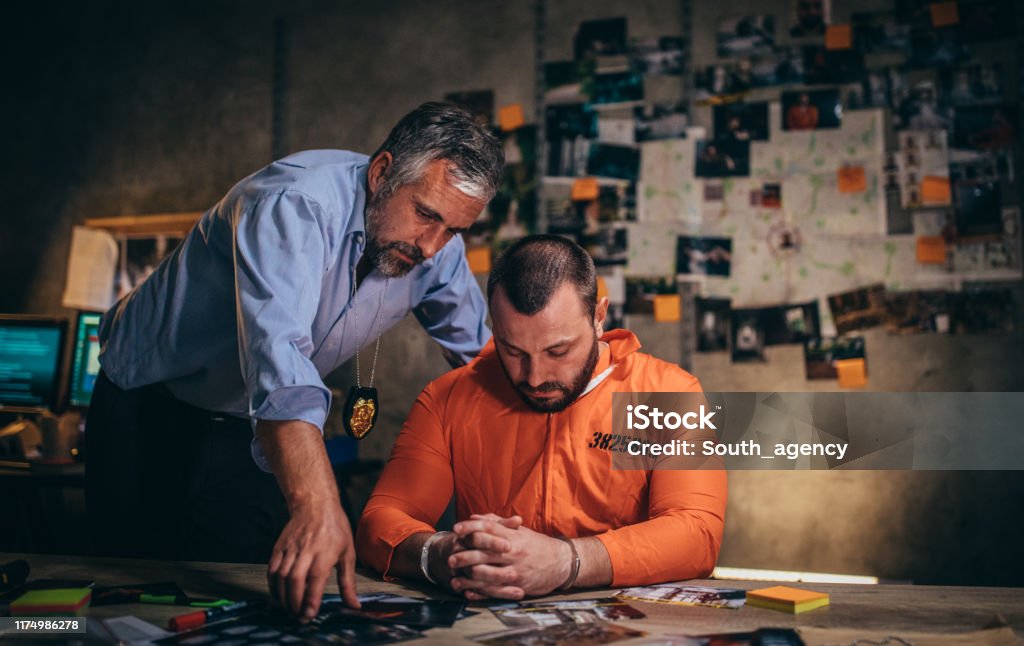 Detective interrogating a prisoner Two men, detective interrogating man prisoner in orange jumpsuit in office. Adult Stock Photo
