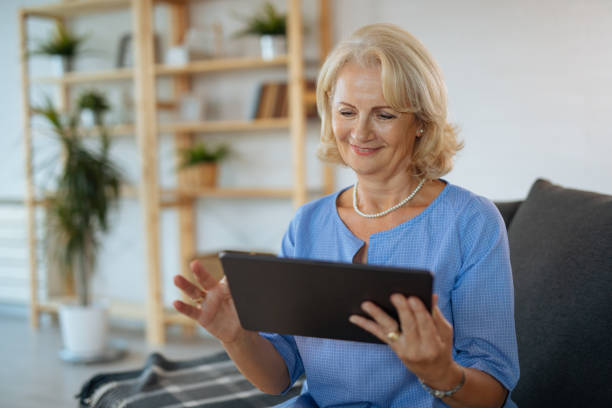 istock Smiling senior woman using digital tablet in living room 1174986707