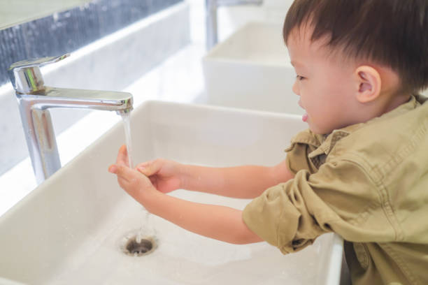 sian 3 - 4歳の幼児の男の子の子供は、公衆トイレの蛇口からシンクと水滴に自分で手を洗います - 3 4 years ストックフォトと画像