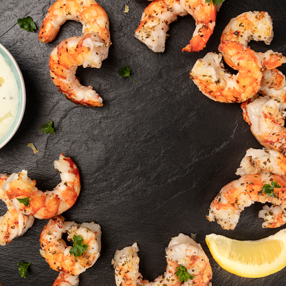 Cooked shrimps with a Caesar sauce and lemon, shot from above on a black background, forming a square frame with a place for text