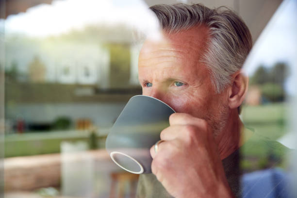 istock Senior Man Standing And Looking Out Of Kitchen Door Drinking Coffee Viewed Through Window 1174998207