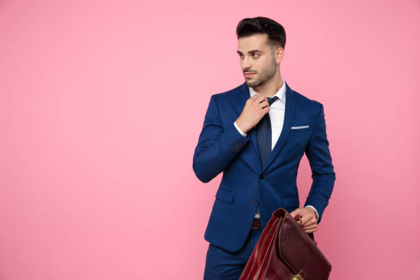 istock confident young man fixing tie and holding suitcase 1174999835