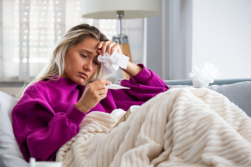 Enfermedad, concepto de problema de virus estacionales. Mujer enferma teniendo gripe tendida en el sofá mirando la temperatura en el termómetro. Mujer enferma acostada en la cama con fiebre alta. Gripe fría y migraña. photo