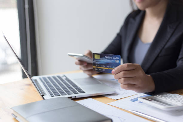 istock Midsection Of Businesswoman Holding Credit Card While Using Phone On Table 1175000232