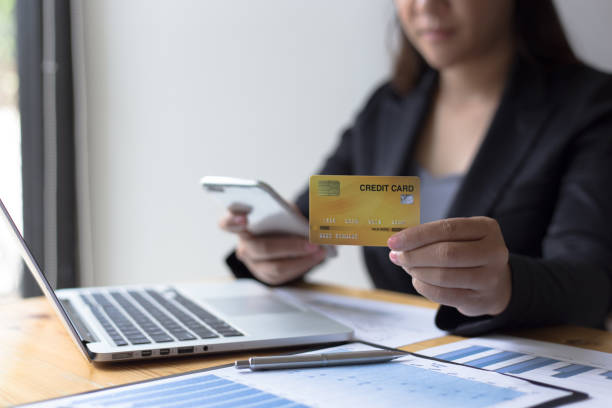 istock Midsection Of Businesswoman Holding Credit Card While Using Phone On Table 1175000235