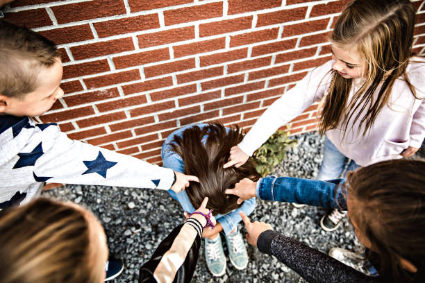 smutny moment zastraszania. dziewczyna siedzieć na ziemi zastraszanie w schoolyard - bullying sneering rejection child zdjęcia i obrazy z banku zdjęć