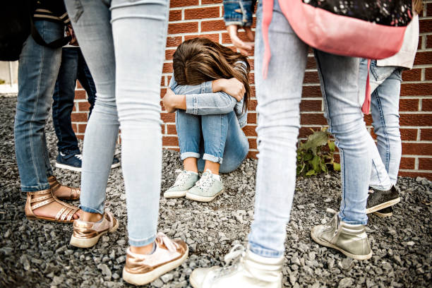 smutny moment zastraszania. dziewczyna siedzieć na ziemi zastraszanie w schoolyard - bullying sneering rejection child zdjęcia i obrazy z banku zdjęć