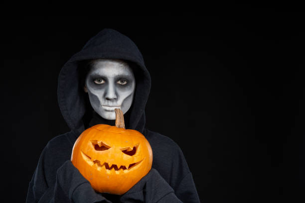 istock Boy with Halloween makeup holding Jack-O-Lantern  pumpkin on black background 1175004321
