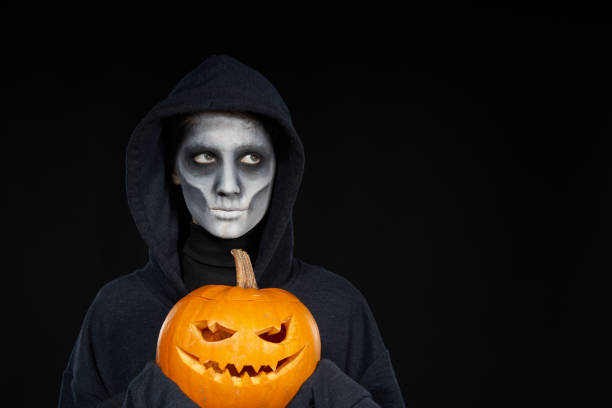 istock Boy with Halloween makeup holding Jack-O-Lantern pumpkin on black background 1175004396
