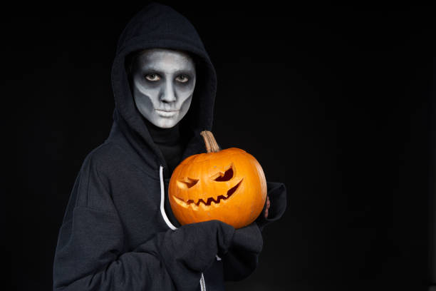 istock Boy with Halloween makeup holding Jack-O-Lantern  pumpkin on black background 1175004445