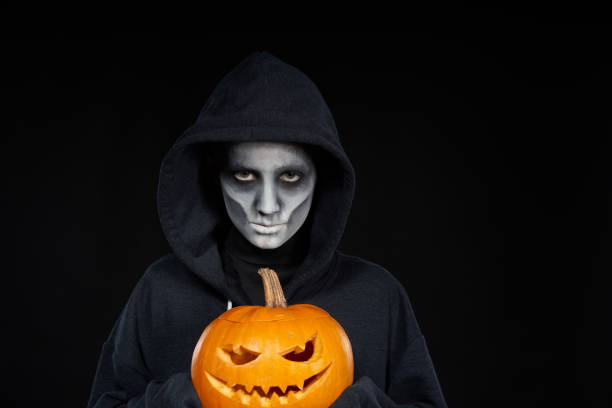 istock Boy with Halloween makeup holding Jack-O-Lantern  pumpkin on black background 1175005052