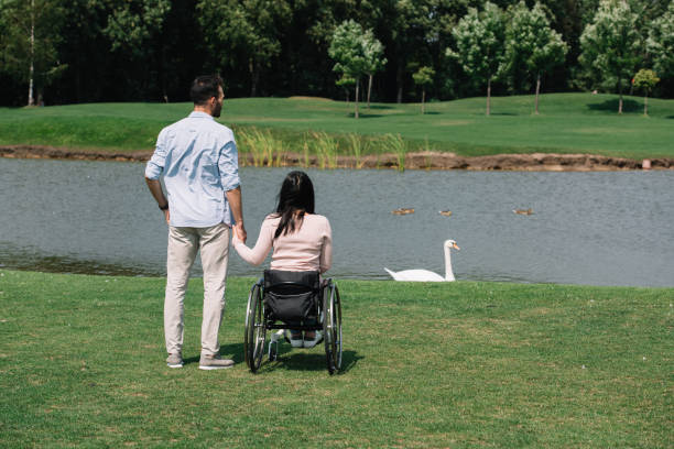 istock back view of young man holding hands with disabled woman while looking at pond in park 1175005202