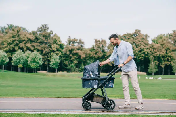 happy father walking with baby pram in green park