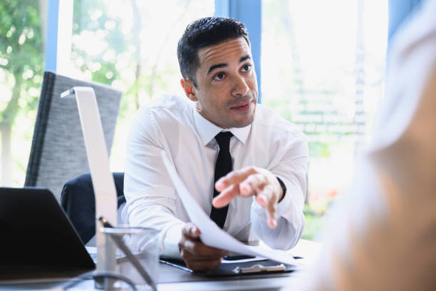 Mid 30s businessman explaining merits of plan to colleague Low angle view of inspired Hispanic businessman in mid 30s sitting across from client and making convincing sales pitch. persuasion stock pictures, royalty-free photos & images