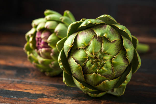 boccioli di fiori di carciofo freschi crudi coltivati biologicamente su tavolo di legno - artichoke food vegetable freshness foto e immagini stock