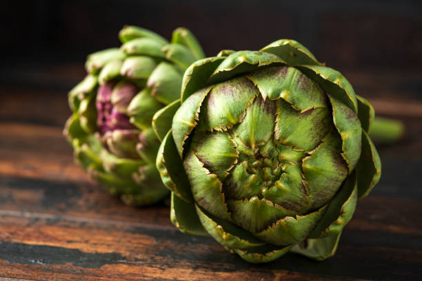 Fresh raw organically grown artichoke flower buds on wooden table Fresh raw organically grown artichoke flower buds on wooden table. artichoke stock pictures, royalty-free photos & images