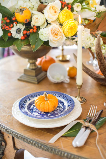 istock Luxurious elegant wedding decor in autumn style. Wooden vintage table setting with ceramic plates and silver cutlery. Fresh flowers in a vase, orange pumpkins, deer horns and candles. Romantic dinner. 1175007910