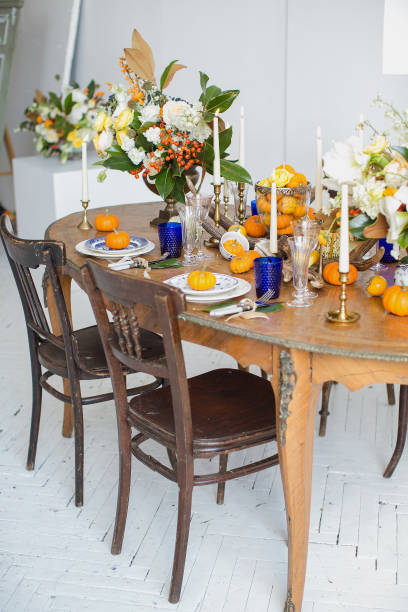 istock Luxurious elegant wedding decor in autumn style. Wooden vintage table and chairs setting with ceramic plates and silver cutlery. Fresh flowers in a vase, orange pumpkins, deer horns and candles. 1175011202