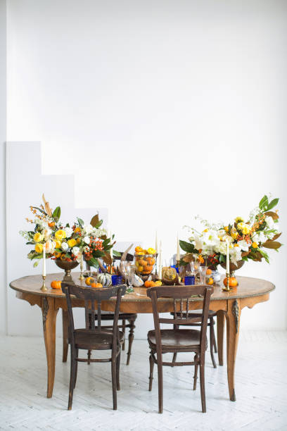 istock Luxurious elegant wedding decor in autumn style. Wooden vintage table and chairs setting with ceramic plates and silver cutlery. Fresh flowers in a vase, orange pumpkins, deer horns and candles. 1175011549