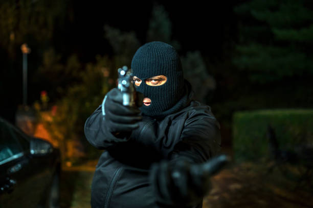 Man in skin mask holding gun A man holding a gun in hand, the ship ready to shoot the man pointed a gun at us. A man holding a gun was robbed. man holding gun at night in the city stock pictures, royalty-free photos & images