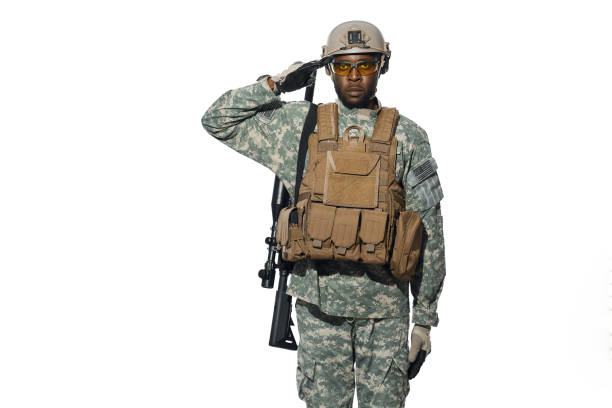 Front view of African male soldier serve in army, hears and executes orders. American soldier wearing uniform with modern weapon machine holding hand near head. White studio background.