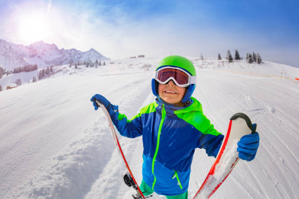 istock Happy boy on skiing slope hold ski look up smiling 1175030128