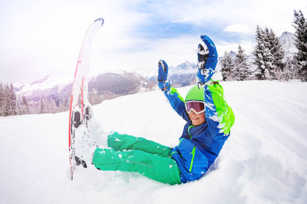 istock Happy boy hold ski sit in snow with lifted hands 1175030154