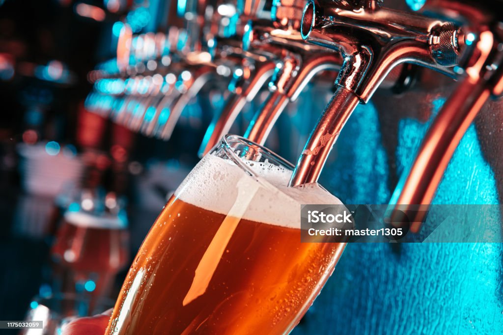 Hand of bartender pouring a large lager beer in tap Hand of bartender pouring a large lager beer in tap. Bright and modern neon light, males hands. Pouring beer for client. Side view of young bartender pouring beer while standing at the bar counter. Beer - Alcohol Stock Photo