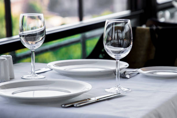 istock Table setting in restaurant terrace with green background. Empty wine glasses, plates, forks, knifes on the tablecloth. Elegant restaurant interior. 1175038913