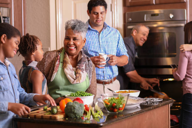 Diverse family in home kitchen cooking Thanksgiving dinner. Multi-ethnic family members work together in grandmother's home kitchen to prepare Thanksgiving dinner.  Hispanic, African and Caucasian ethnicities.  Roasted turkey, vegetable food items. Oven in background. family dinners and cooking stock pictures, royalty-free photos & images