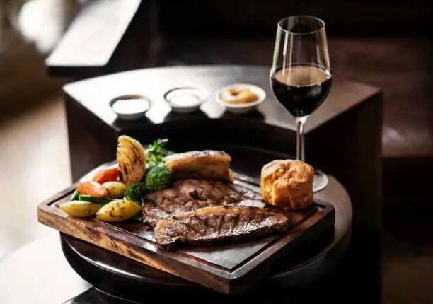 Photo of gourmet sunday roast beef traditional british meal set on old wooden pub table with glass of red wine