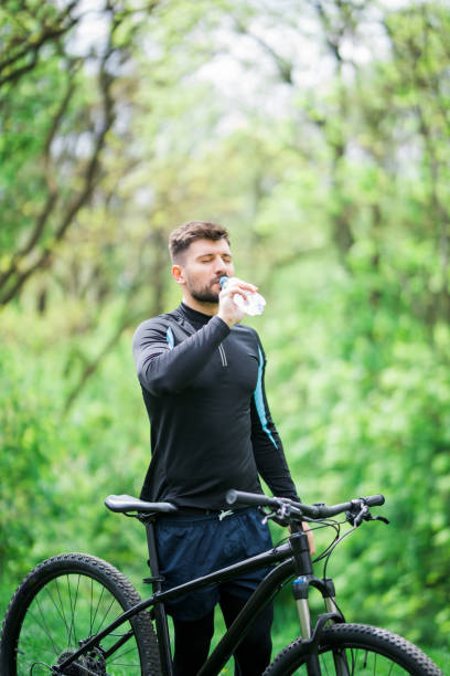 istock Tired biker resting and drinking from water bottle in green park 1175041549