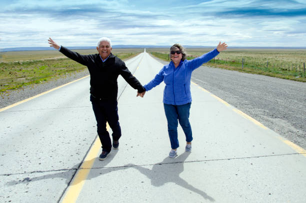 A fun and loving senior couple are holding hands, and  standing on a road in the Chilean Patagonia.