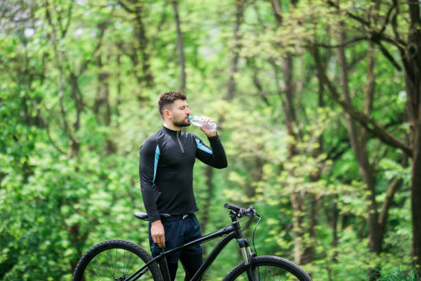 istock Young man in track-suit with bicycle drinking water at summer park 1175043131