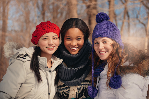 Group of millenial young female adult friends enjoying wintertime and in a snow filled park