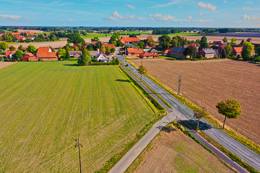 Aerial view of a straight country road leading to a village in a cultural landscape of monotonous arable land.