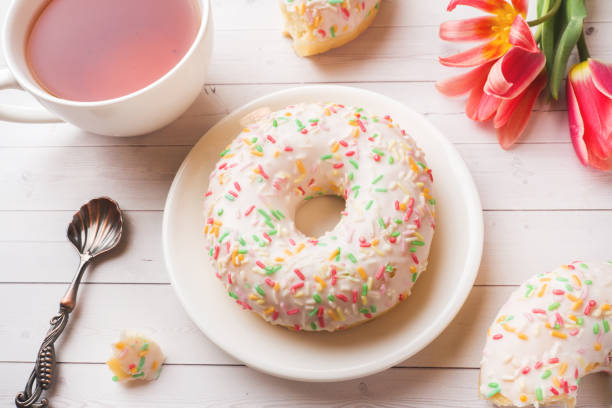 istock Cup of tea and donuts, flowers tulips on white table with copy space. 1175047655