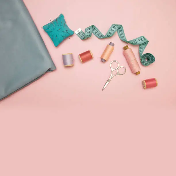 Sewing accessories and fabric on a pink background. Sewing threads, needles, fabric, buttons and sewing centimeter. top view, flat lay