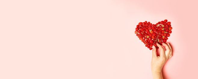 Assorted ripe red berries of raspberries, currants and strawberries, and a female hand takes a berry on a pink background. Summer food concept